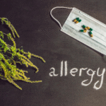 white mask with green and yellow capsules scattered on top of it, on the left side of greenery is visible, and below the mask, the word allergy is written