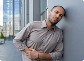 A man stands in front of a building, clutching his stomach in discomfort, indicating upper abdominal pain.