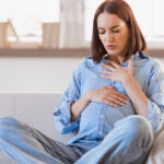 Pregnant woman sitting on a couch, hands on her stomach, visibly experiencing breathing problems in pregnancy.