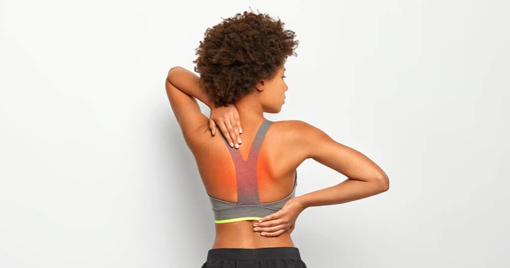 A woman suffering from upper back pain, holding her shoulder and appearing visibly uncomfortable.