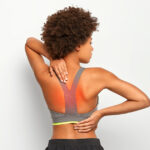 A woman suffering from upper back pain, holding her shoulder and appearing visibly uncomfortable.