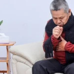 Elderly man coughing indoors showing common pneumonia symptoms.