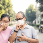 Older couple coughing outdoors while showing pneumonia-like symptoms.