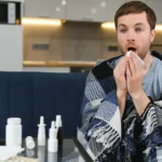 Sick man coughing on couch with tissues and medicine