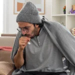 Sick man coughing at home while seeking wheezing relief.